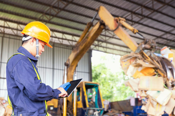Engineer driving a loader in the recycling plant. Factory recycle workers are using a tablet to control work in the recycling plant.