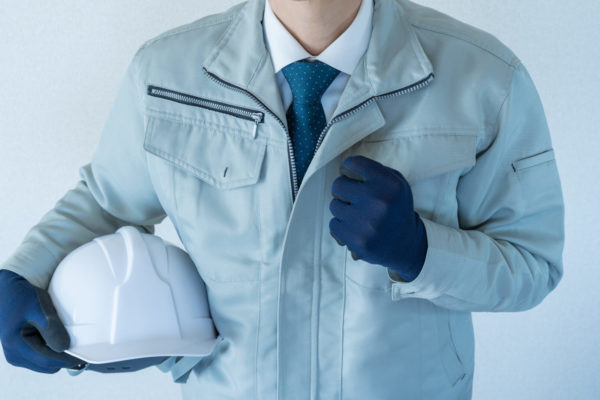 作業服にネクタイの男性。ヘルメットを抱える